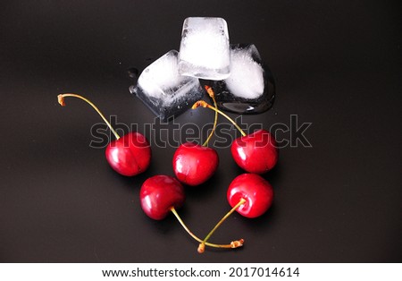 A pile of ripe cherries and cubes of melted ice on a black background. View from above.