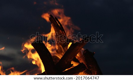 A close up of golden flames of a bonfire in the sky. Macro shot of yellow and orange fire flaring on firewood in the night. Relaxing near the fireplace, getting warm and cozy.