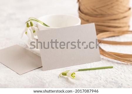 Gray paper invitation card, mockup with galanthus snowdrop flowers on gray concrete background. Blank, side view, still life, copy space, wedding invitation.