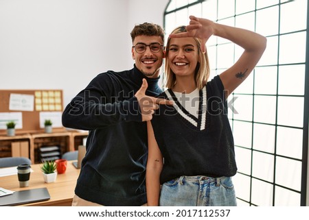 Two beautiful business workers wearing business style standing at the office smiling making frame with hands and fingers with happy face. creativity and photography concept. 
