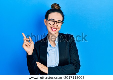 Young hispanic girl wearing business clothes and glasses with a big smile on face, pointing with hand and finger to the side looking at the camera. 