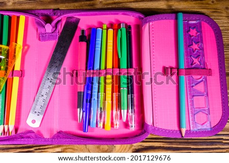 Different school stationeries (pens, pencils, ruler and protractor) in pink pencil box. Top view