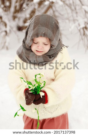 a fairy tale of 12 months. girl with snowdrops in a snowy forest in a warm white shawl, brown skirt with a basket. vertical photo. large portrait