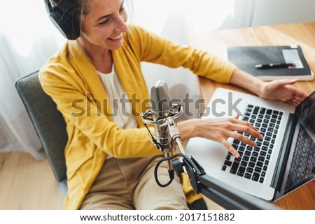 Woman sits with put your feet on table and recording podcast at his small cozy radio studio. Female podcaster streaming her voice into microphone