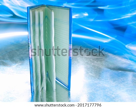 Small note book diary presented around blueish light effect with reflection.