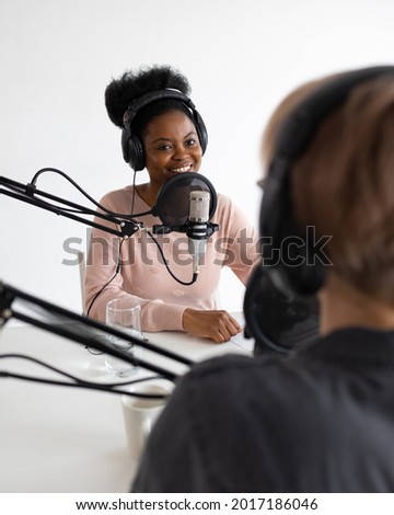 Podcasters, African American and European woman with headphones and microphone recording a podcast in a recording studio, Millennial black woman and white woman creating audio content, confident women