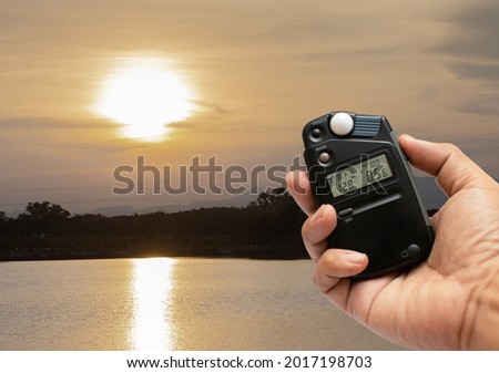 Photographers use light meters to measure correct exposure settings in landscapes at sunset.