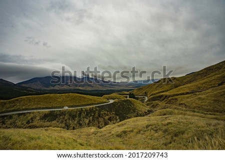 Winding road through the mountain in Japan with cloudy sky and green-yellow grass over hill. View of road through complex moumtain scene from view point.