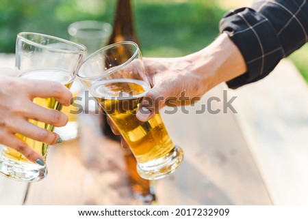 Cropped shot of people holding beer glasses celebrating in the summer camping party outdoor. Friends clinking bottle of beer during camping outdoor