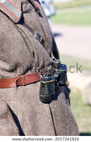 Old black military binoculars on the background of an army overcoat