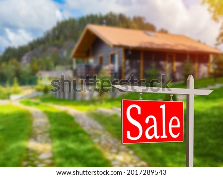 Sell sign near house. Red sell sign near cottage. Sale of country cottage. Country house with inscription sell. Sale of suburban real estate. House at foot of mountain. Selective focusing.