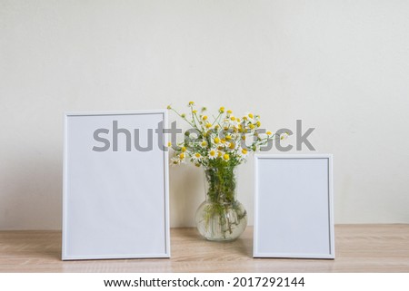 Portrait white picture frame mockup on wooden table. Glass vase with camomile