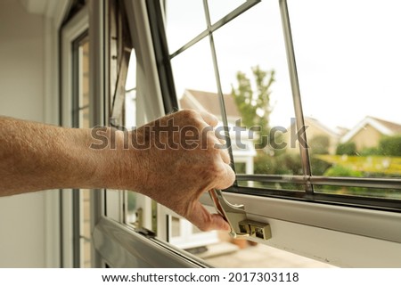 Homeowner seen about to lock a double glazed window seen on the ground level of a property. The latch can itself be locked to enhance security.