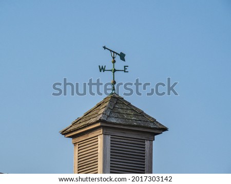 a simple arrow weather vane pointing West on a shingles roof copula on a country building