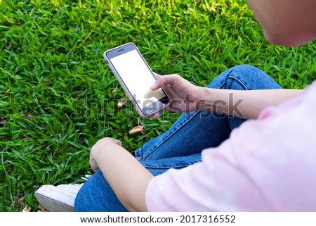 Woman's hand holding black mobile phone with blank desktop screen. empty screen for mockup image or advertisement. while sitting on the lawn in an outdoor park. close up view.