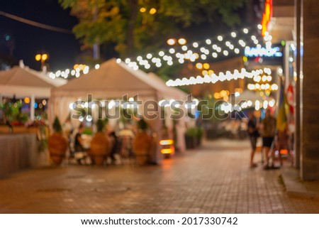 Blurred abstract background of outdoor cafe or restaurant. Outdoor cafe with tables and chairs. Street cafe in the evening in Kiev. Customers sit at tables in a terrace area outside cafe