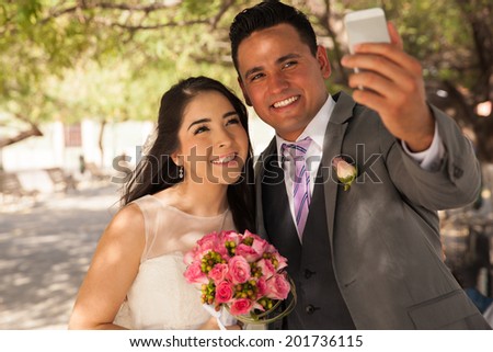 Beautiful Hispanic bride and groom taking a selfie with a mobile phone outdoors