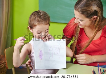 Proud girl showing her drawing to nursery teacher in kindergarten