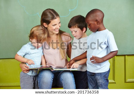 Happy child day care worker with children reading a book in kindergarten
