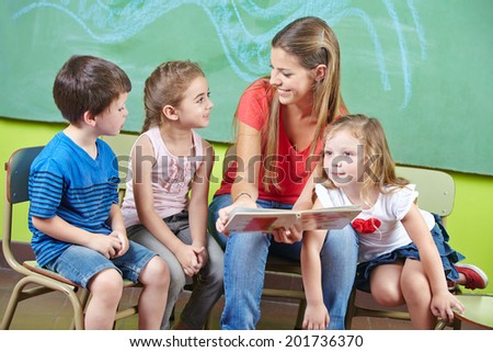 Child care worker and children reading a picture book together in a kindergarten