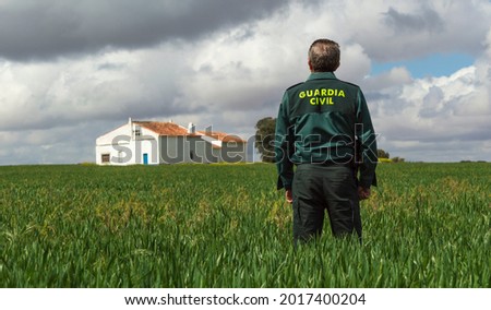 A Spanish civil guard watches over a country house from a grassy field. Royalty-Free Stock Photo #2017400204