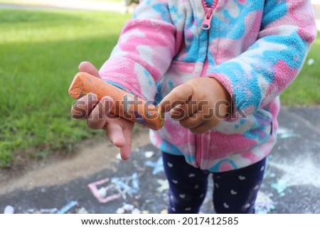 Young toddler girl playing outside with chalk refining her fine motor skills as well as working on colour recognition, letters and numbers