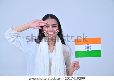 Teenage girl saluting and holding Indian flag in Patriotic mood on the Occasion of Independence Day India celebrations studio shot Royalty-Free Stock Photo #2017419299