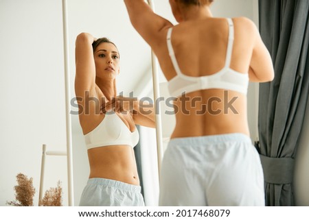 Cancer aware young woman looking herself in a mirror while doing breast self-examination at home.  Royalty-Free Stock Photo #2017468079