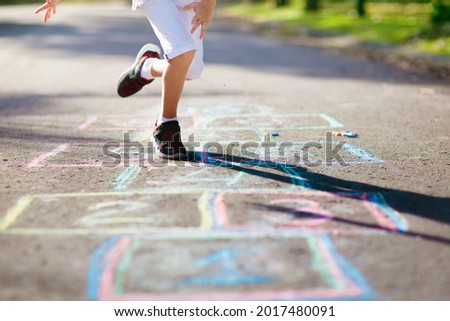 Kids play hopscotch in summer park. Healthy active outdoor game. Children playing and drawing with chalk on suburban city street. Boy and girl jump. Hop scotch fun for young child. Kid jumping. Royalty-Free Stock Photo #2017480091