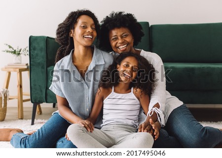 Cheerful woman with her two daughters at home. Mature woman sitting in living room with her daughters looking at camera and smiling. Royalty-Free Stock Photo #2017495046