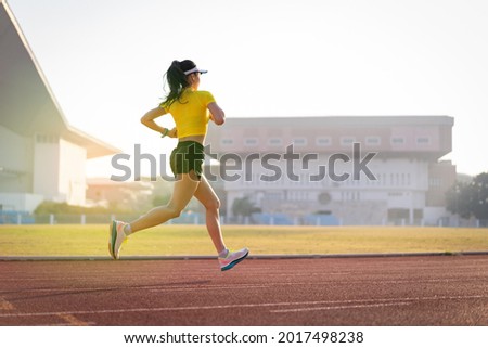 A young Asian woman athlete runner jogging on running track in city stadium in the sunny morning to keep fitness and healthy lifestyle. Young fitness woman runs on stadium track. Sport and recreation