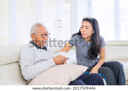 Picture of old man holding a cup of tea while talking together with his daughter in the living room at home