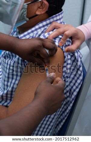 A nurse is injecting vaccine to left shoulder of a male patient, during Covid-19 mass vaccination program. A close-up and selective focus photo of nurse fingers, needle and syringe. 