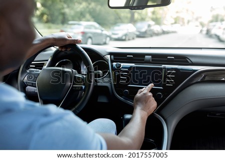 Technologies and modern cars concept. Cropped of black guy driver using touch pad with blank screen on automobile dashboard, using navigation while driving, mockup, over shoulder shot Royalty-Free Stock Photo #2017557005