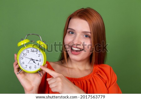 Young red hair woman in casual orange blouse on green background holding alarm clock happy cheerful excited smiling