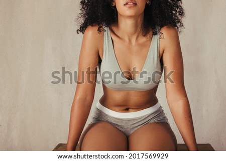Anonymous female model posing confidently in her natural body.  Body positive young woman wearing underwear and sitting alone against a fabric background. Royalty-Free Stock Photo #2017569929