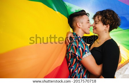 Affectionate  couple bonding against a rainbow pride flag. Young LGBTQ couple embracing each other and touching their noses together. Two non-conforming lovers smiling while standing together. Royalty-Free Stock Photo #2017570718