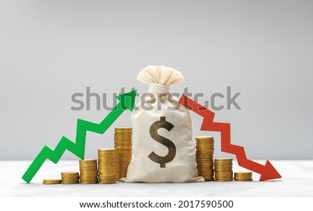 Money bag with daollar sign. Graph is growing green arrow up and graph of falling red arrow down on the background of a stack of coins. Market fluctuation concept. Royalty-Free Stock Photo #2017590500