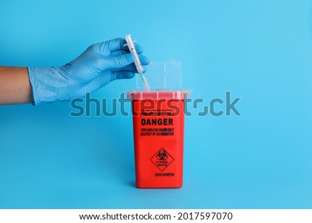 Doctor throwing used syringe into sharps container on light blue background, closeup Royalty-Free Stock Photo #2017597070