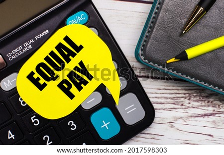 On a light wooden table, there is a calculator, a notebook, a pen, a yellow pencil, and a yellow card with the text EQUAL PAY. Business concept.