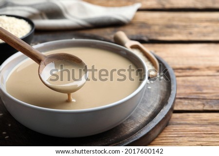Spoon with tasty sesame paste over bowl on wooden table, closeup Royalty-Free Stock Photo #2017600142