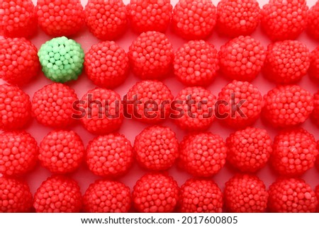 Delicious green gummy raspberry candy among red ones on pink background, flat lay