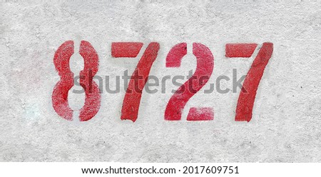 Red Number 8727 on the white wall. Spray paint. Number eight thousand seven hundred and twenty seven.