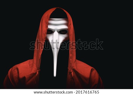 Mystic red hooded person in white mask. Man in red ritual cloak. Satanic ,occult, esoteric and black magic concept. Copy space. Royalty-Free Stock Photo #2017616765