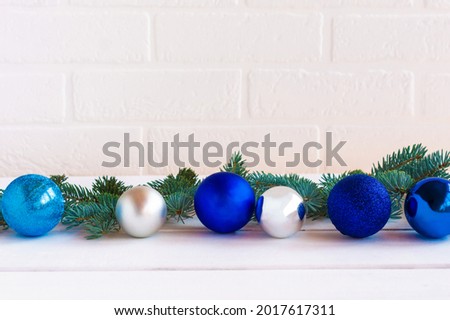 Christmas composition with blue and silfer baubles and fir tree brances on white brick wall background with copy space for text.