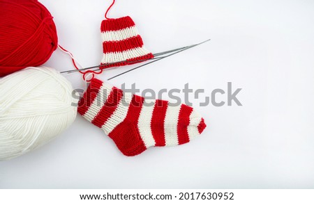 Knitting a warm sock red and white yarn on five knitting needles. Yarn and metal knitting needles on a white background. The concept of Hobbies, home production, and individual entrepreneurship.