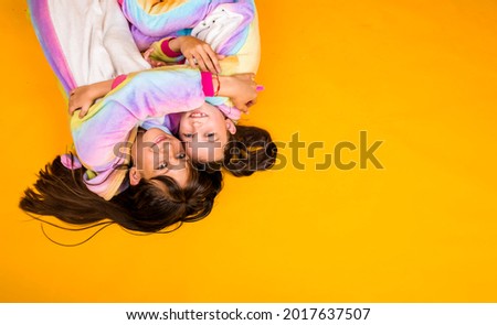happy girlfriends in plush suits jumpsuits lie on a yellow background with a place for text