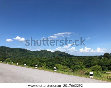 Sunny blue sky against green forest and local asphalt road in summer of Thailand. Fresh oxygen area and relaxing time view.