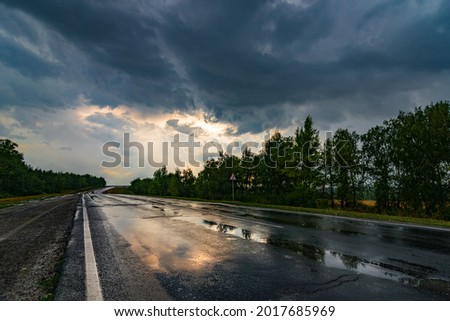 wet asphalt road panorama in countryside on rainy summer day. autumn rain road puddle in forest under dramatic cloudy sky Royalty-Free Stock Photo #2017685969
