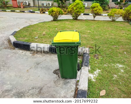 The trash can at the end of the field is green and the lid is yellow
